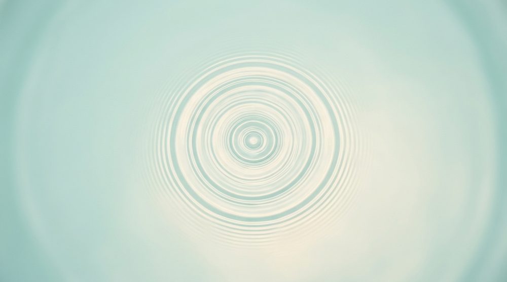 A single ripple spreading across still, pale water
